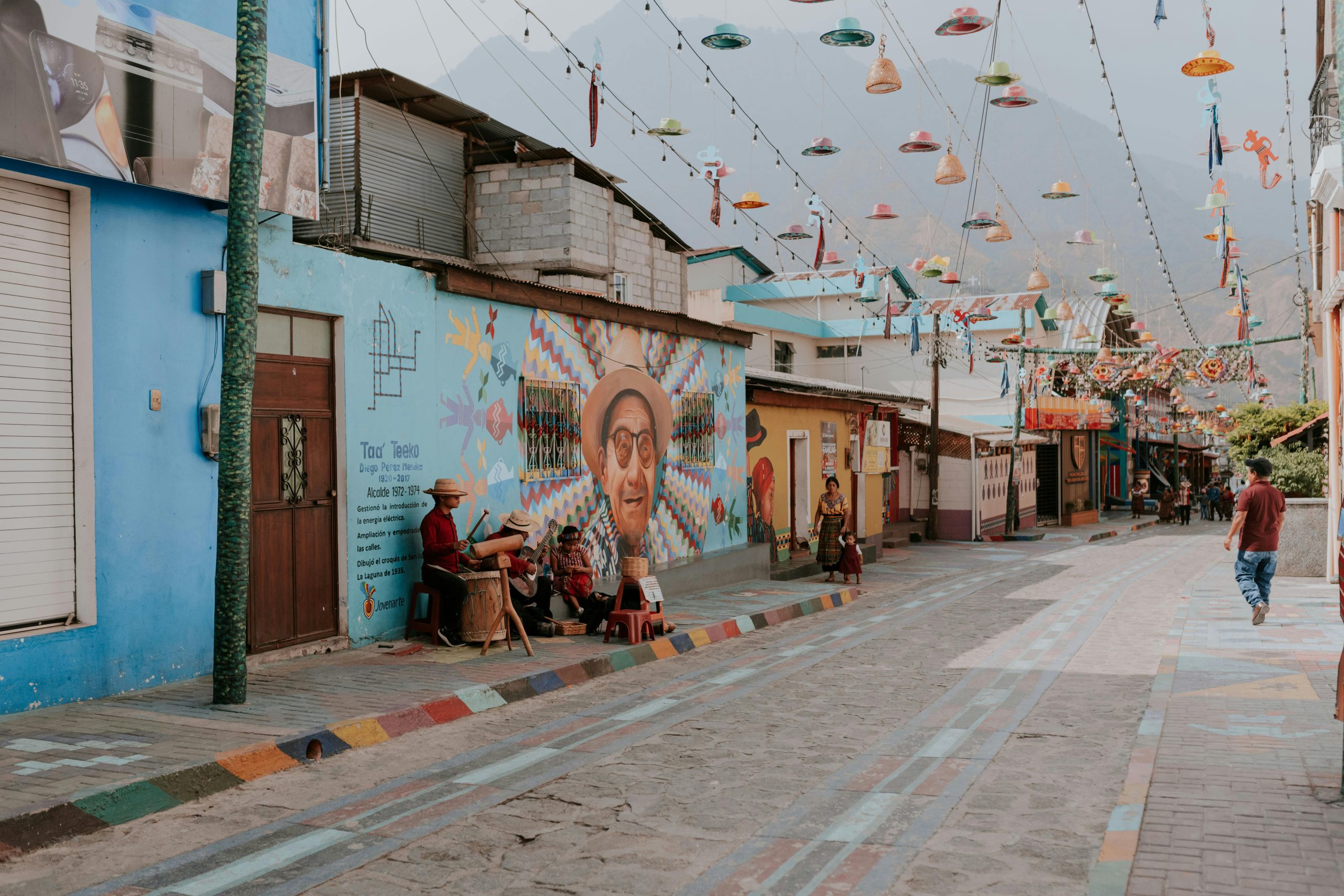 A lively street adorned with colorful murals and hanging decorations in a quaint neighborhood.
