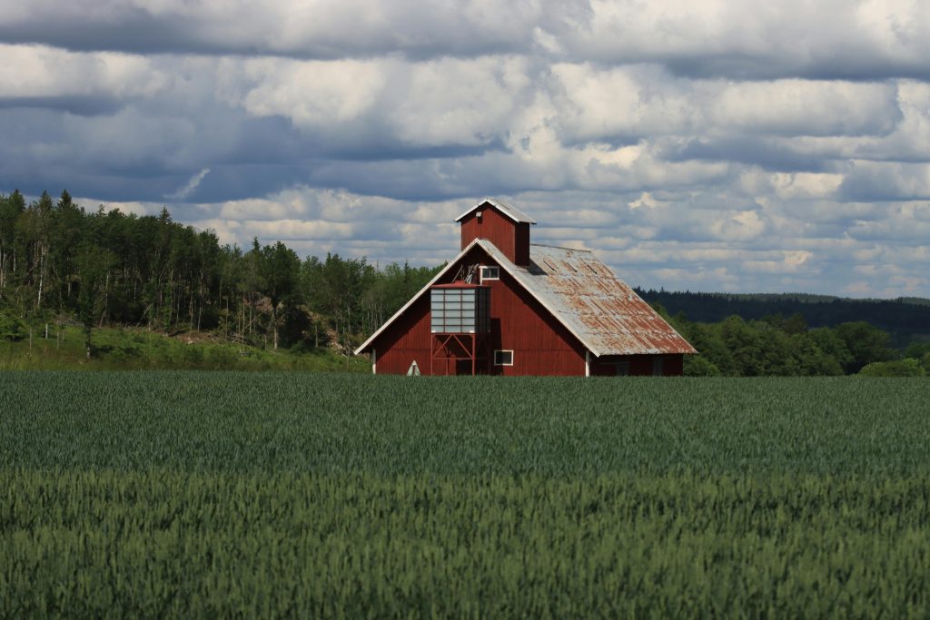 Idyllic red barn surrounded by lush green fields and cloudy skies in Jönköping, Sweden.