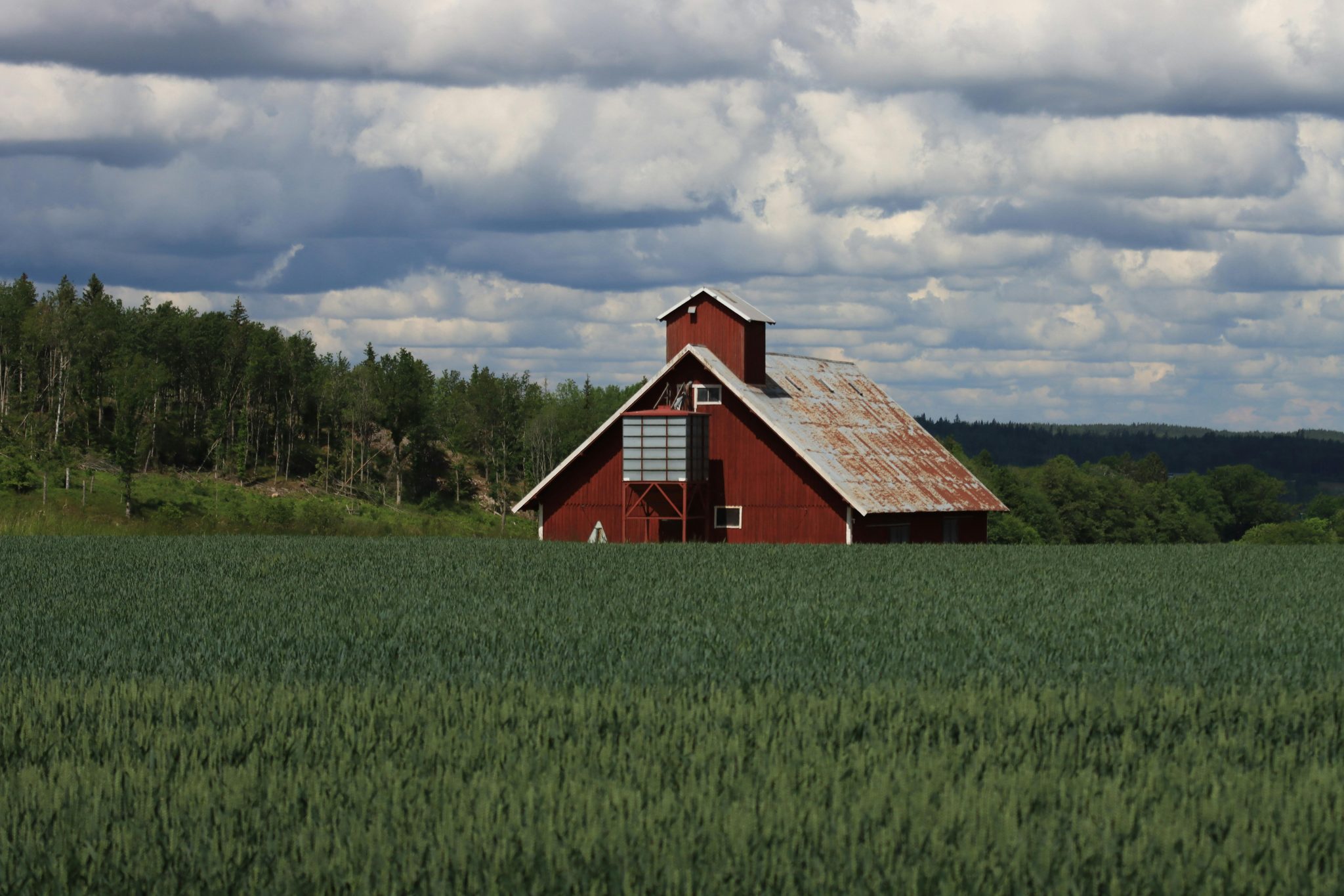 Idyllic red barn surrounded by lush green fields and cloudy skies in Jönköping, Sweden.
