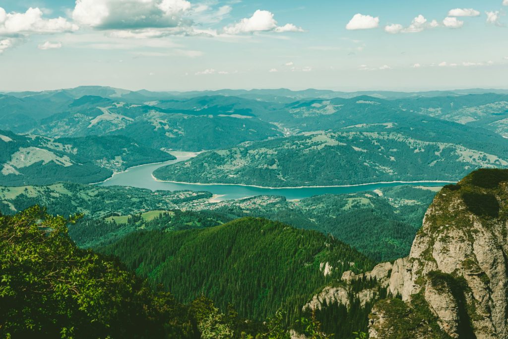 Expansive vista of a lush mountain valley with a winding river under a bright sky.