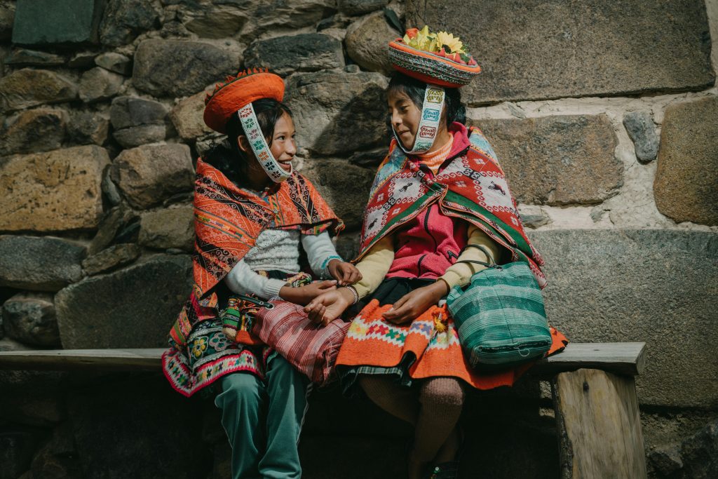 Two Peruvian women in vibrant traditional clothing sharing a moment in Ollantaytambo, Peru.