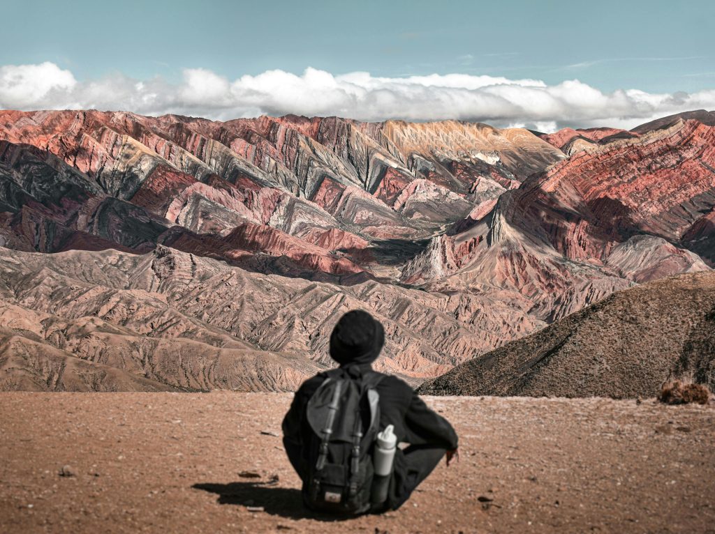 A traveler sits facing the colorful mountain range in Humahuaca, Jujuy, Argentina.