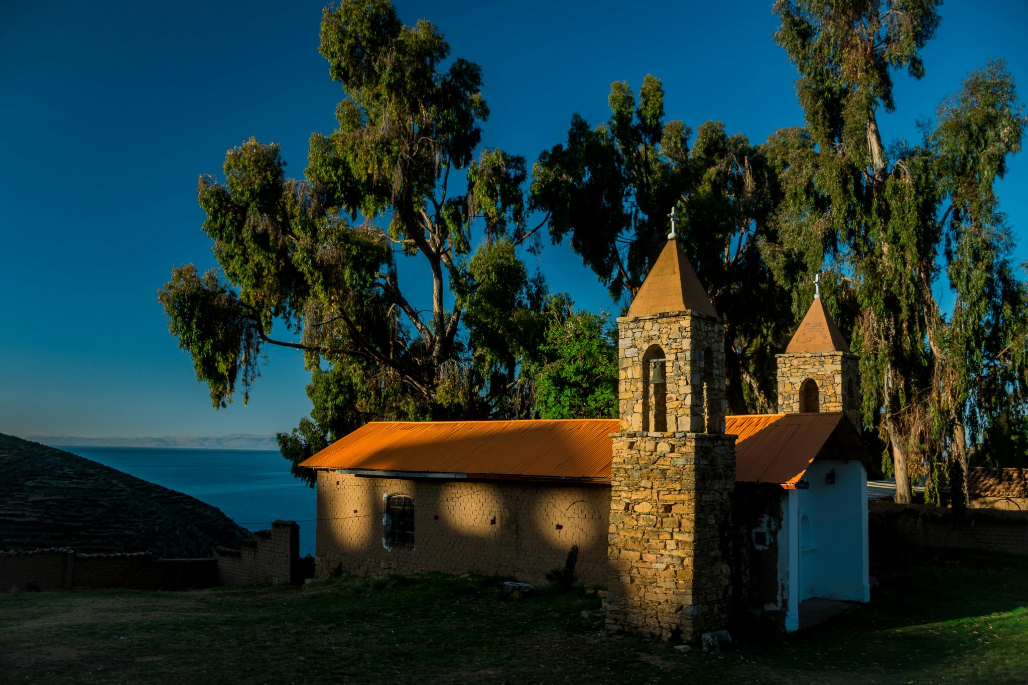Charming stone chapel surrounded by trees on the shores of Lake Titicaca under the warm sunlight.
