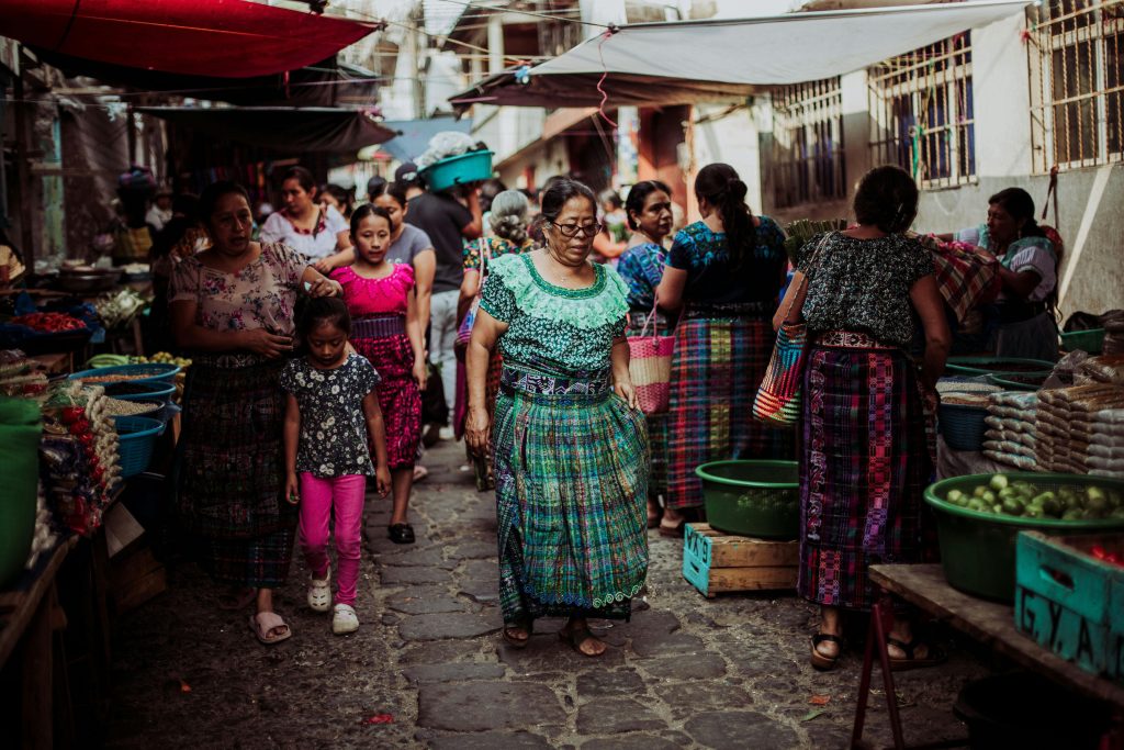 Women and children in colorful traditional dresses at a bustling Guatemalan market.