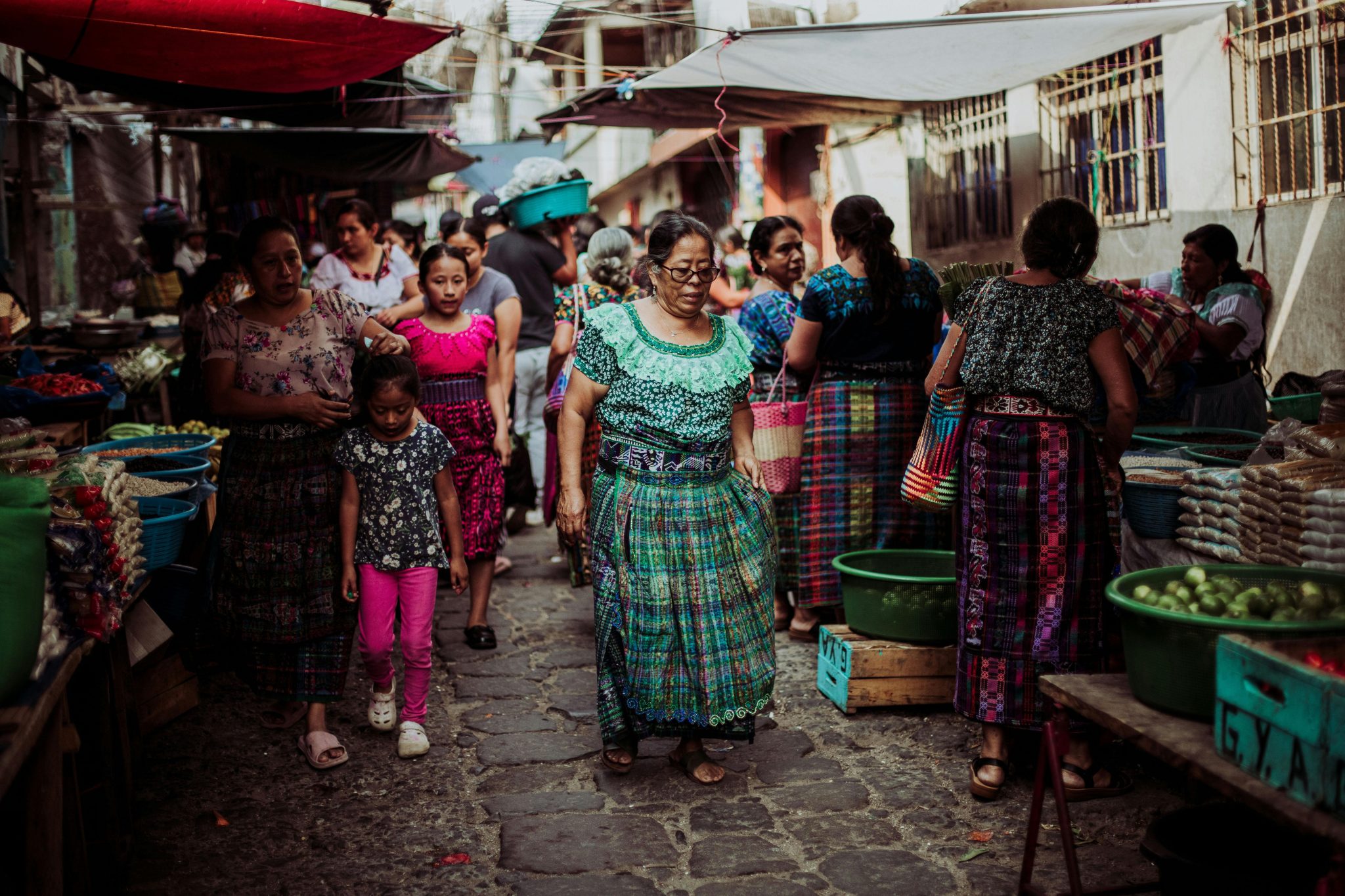 Women and children in colorful traditional dresses at a bustling Guatemalan market.