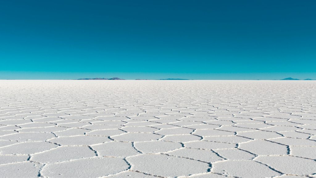 Vast salar with geometric patterns under a clear blue sky in Bolivia's Uyuni.