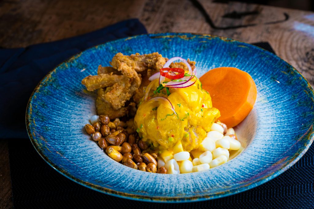 A vibrant Peruvian causa rellena accompanied by crispy fried chicken, potatoes, and corn.