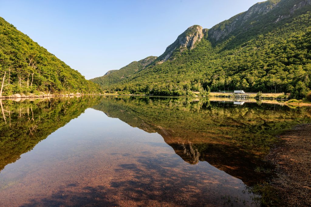Captivating summer scene of a tranquil lake reflecting lush green mountains in Franconia Notch, New Hampshire.
