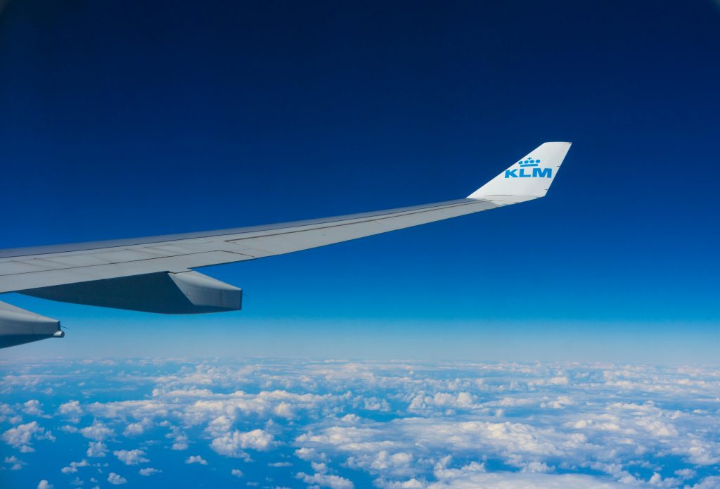 View of an airplane wing flying high above the clouds against a clear blue sky.
