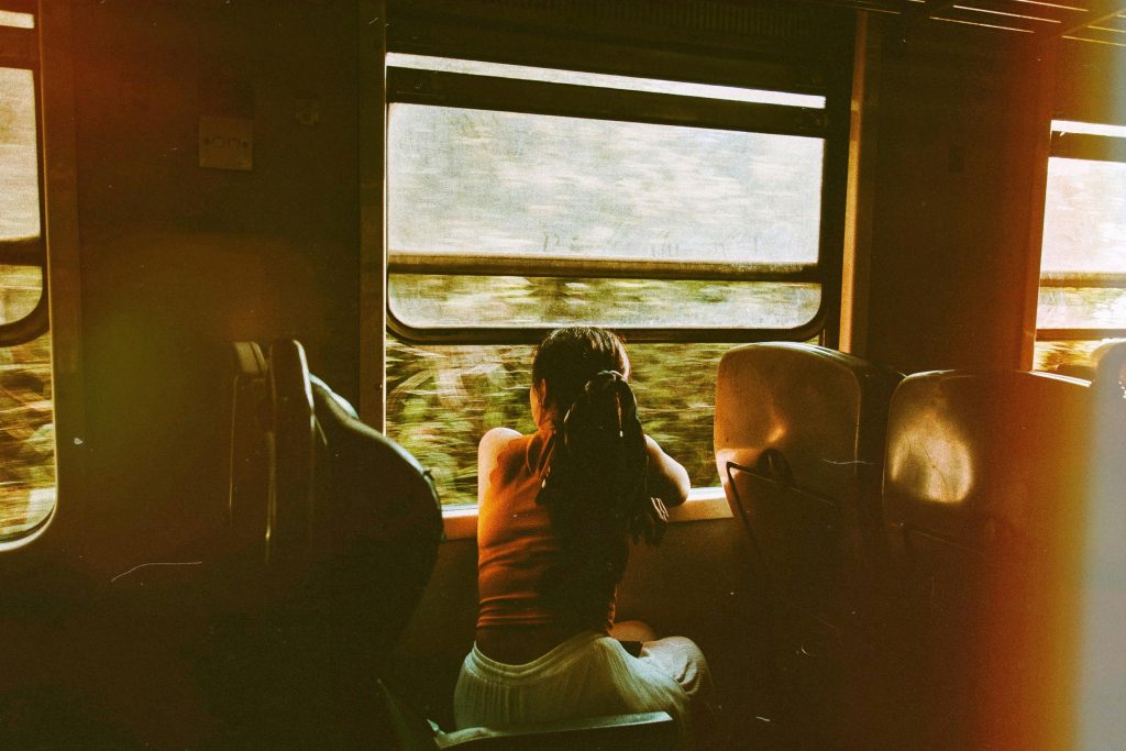 A woman gazes out of a train window, enjoying a serene journey through lush scenery.