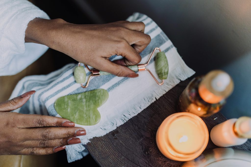 Overhead view of hands using a jade roller in a calming skincare routine with candles.