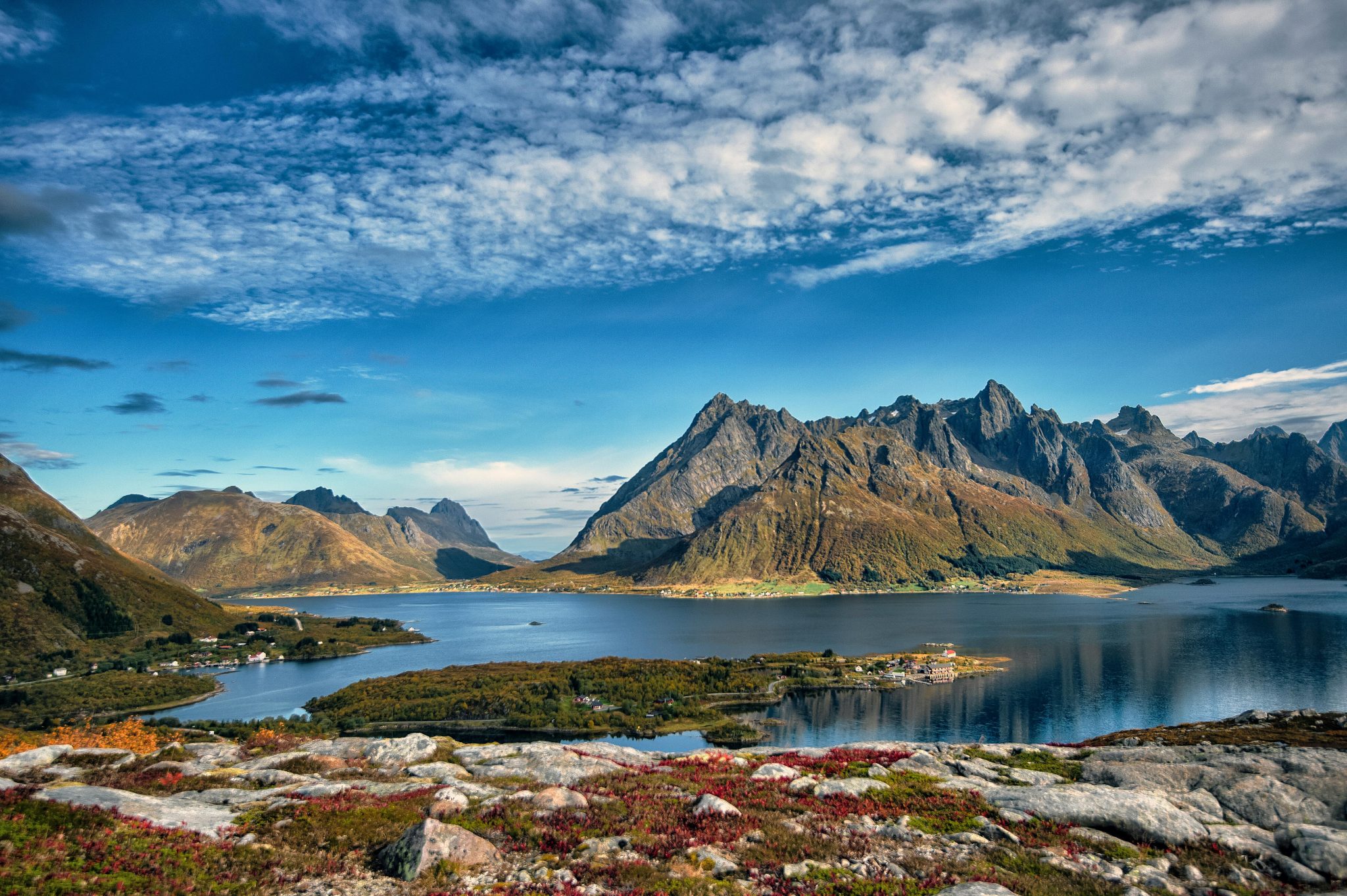 A picturesque view of Lofoten Islands' mountains and serene fjord, under a vibrant sky in Nordland, Norway.